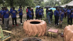 People in blue-and-yellow T-shirts, some with umbrellas, standing around painted tires