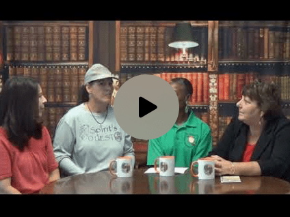 Four women sitting at a table in front of a bookshelf