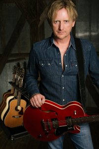 Man in denim pants and denim shirt holding red guitar